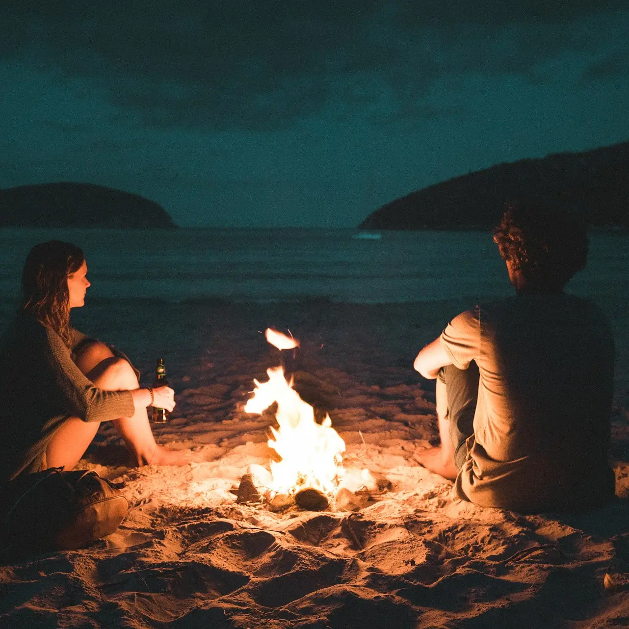 man and woman with bone fire sitting on seashore